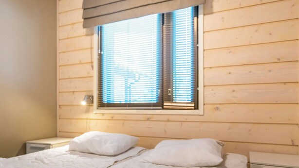 Habitación con paneles de madera, una cama, dos almohadas, una mesita de noche y una ventana con persianas.