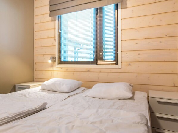 A wooden-paneled room with a bed, two pillows, a nightstand, and a window with blinds.