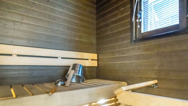 A sauna with wooden benches and a metal bucket.