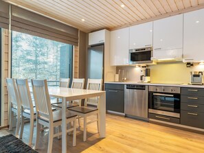 A modern kitchen with a dining area, featuring stainless steel appliances, white cabinetry, and a wooden floor.