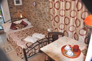Ein Schlafzimmer mit einer Steinsandsteinwand, einem Bett mit gemusterten Betttextilien, einem Tisch mit einer Teewanne und einem Stuhl.