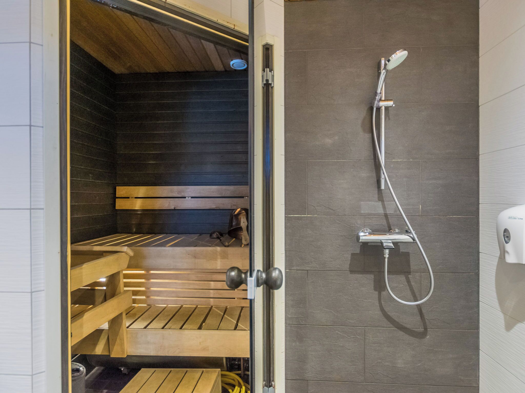 En sauna med træbænke, bruser og sæbedispenser.