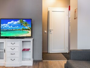 A room with a television displaying a beach scene, a white cabinet with drawers, a closed door, and a patterned sofa.