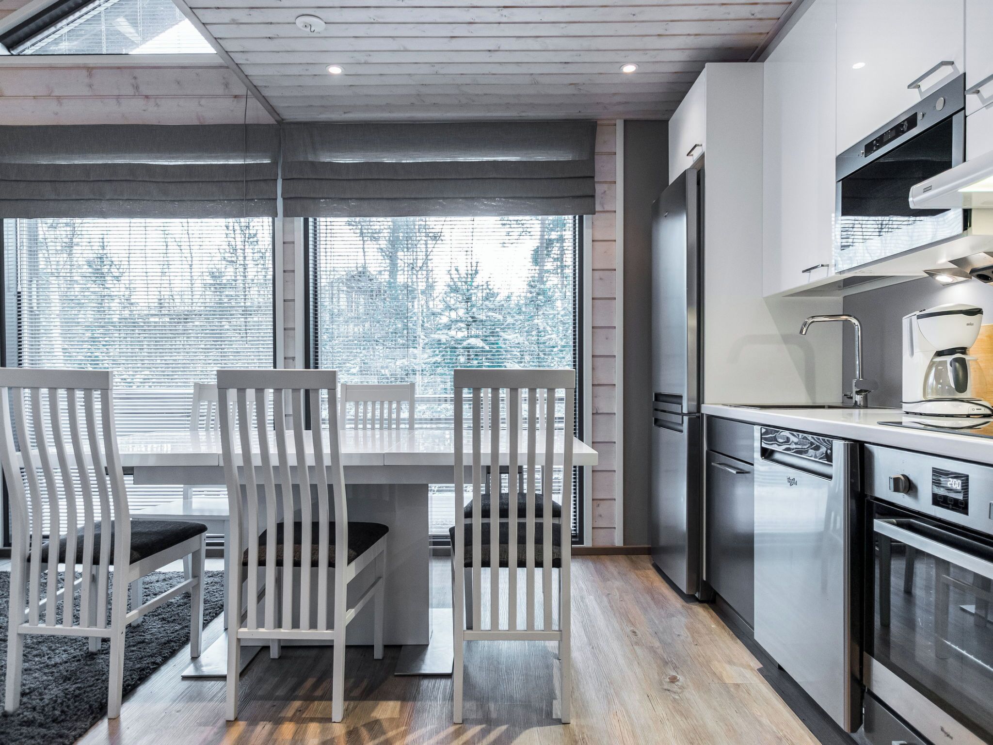 A modern kitchen with a dining area, featuring a large window, stainless steel appliances, and a wooden floor.