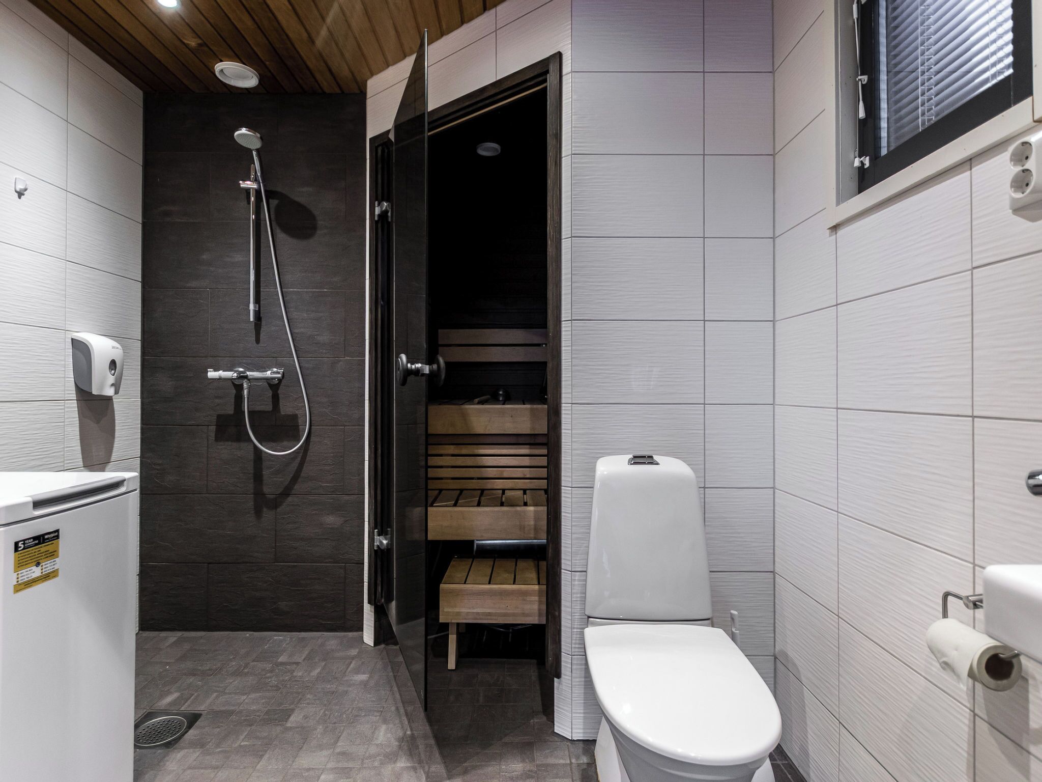 Een moderne badkamer met een douche, toilet en een klein houten bankje.