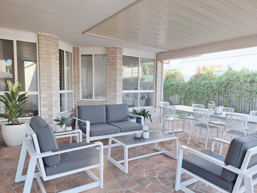 Een terras buiten met witte meubels, waaronder een bank en stoelen, en een tafel.