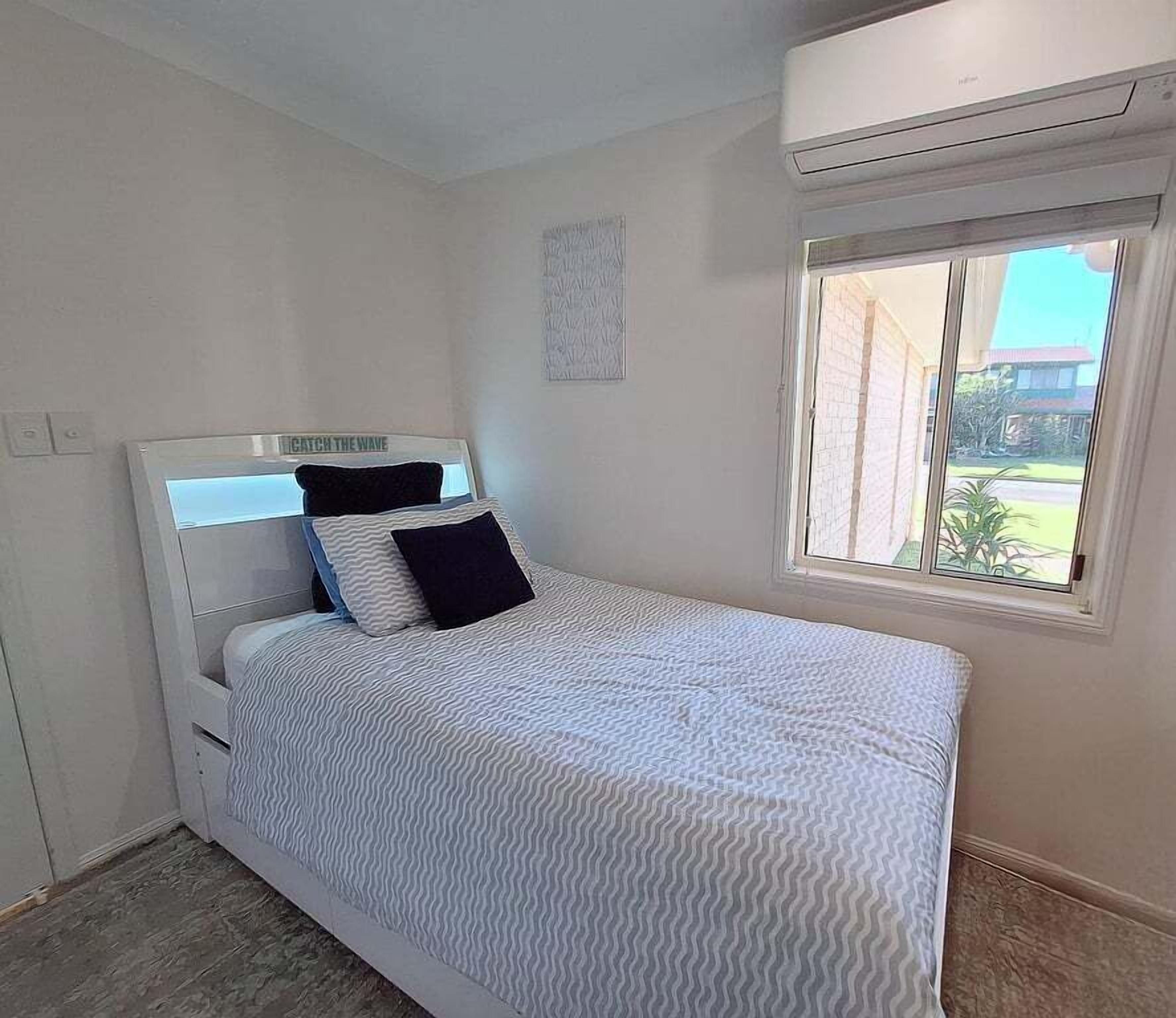 Une chambre à coucher avec un lit, une fenêtre et un climatiseur fixé au mur.