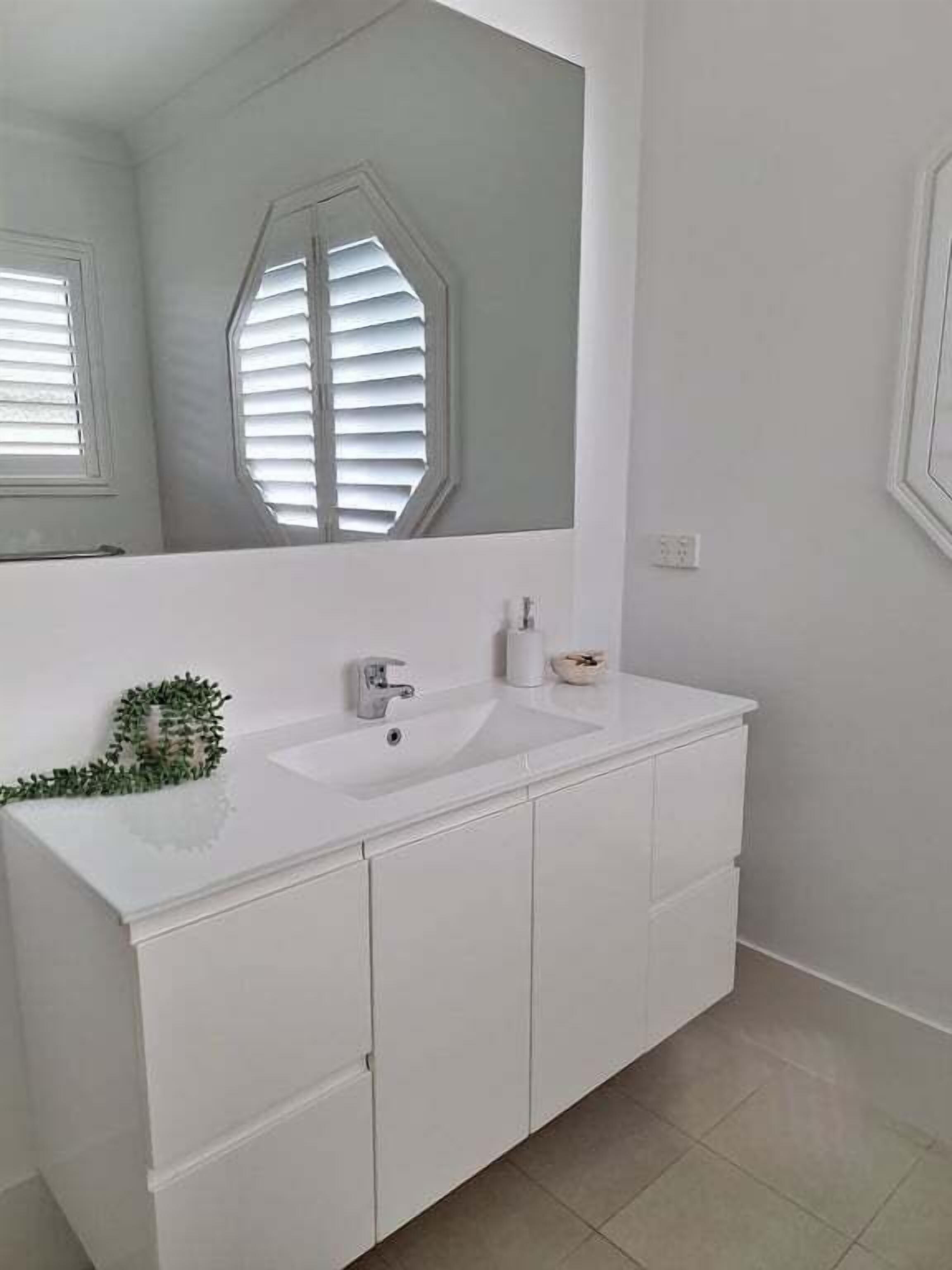 A bathroom with a white vanity, a large mirror, and a window with blinds.