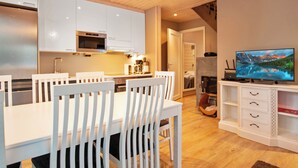 Una cocina moderna con armarios blancos, un comedor con sillas blancas, un televisor de pantalla plana y una chimenea.