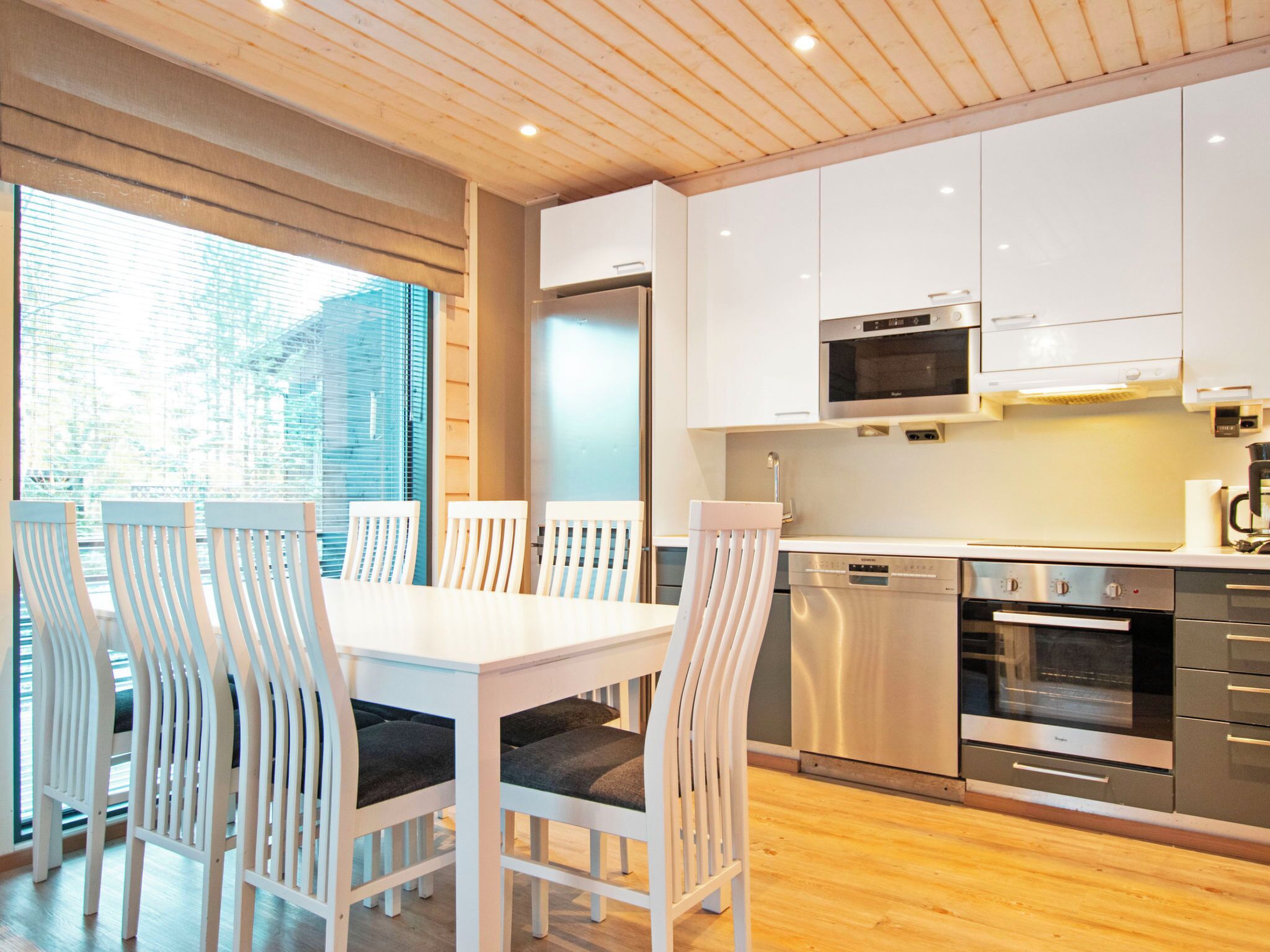 A modern kitchen with white cabinets, stainless steel appliances, and a dining area with white chairs.