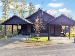 A cabin with two attached structures, a covered porch, and a small tree in front.