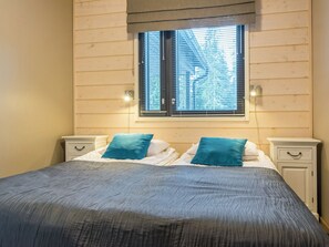 A bedroom with a bed, two nightstands, a window with blinds, and a wall-mounted light fixture.