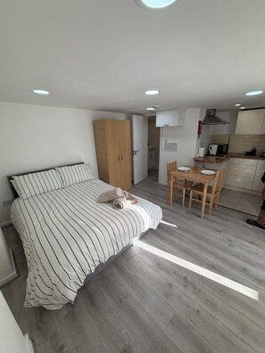 A bedroom with a bed, a wooden wardrobe, and a kitchenette with a dining table and chairs. - Cosy studio in Finsbury Park, 18 minutes from Central London (London)