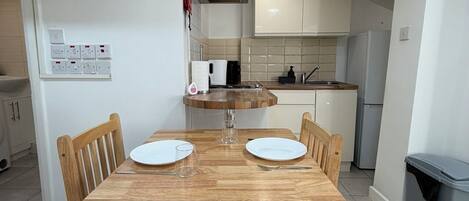A compact kitchen with a dining table, chairs, and a trash bin.