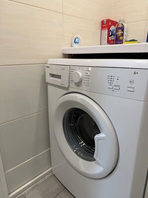 Eine Waschmaschine mit Frontöffnung, deren Oberseite ein Waschmittelbehälter und eine Flasche Weichspüler zeigt.