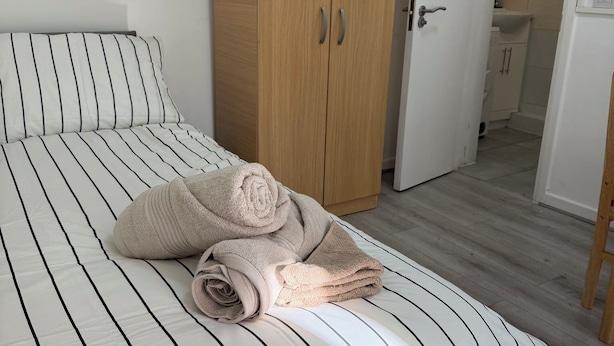 A bedroom with a bed, a wooden wardrobe, and a bathroom visible through an open door. - Cosy studio in Finsbury Park, 18 minutes from Central London (London)
