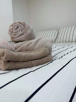 A bed with a striped white and black bedding, a beige towel, and a pillow with a striped pattern. - Cosy studio in Finsbury Park, 18 minutes from Central London (London)