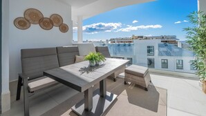 Ein Balkon mit Sofa, Tisch und Blumentöpfen, mit Blick auf die Stadt.