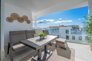 Ein Balkon mit Sofa, Tisch und Blumentöpfen, mit Blick auf die Stadt.