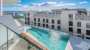 A modern building with a rooftop pool, large windows, and a view of the sea.