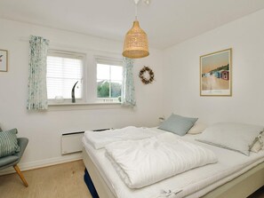 A bedroom with a bed, a chair, a window with curtains, a wall-mounted light fixture, and a framed picture. - 4 Star Holiday Home in Vejby (Vejby)