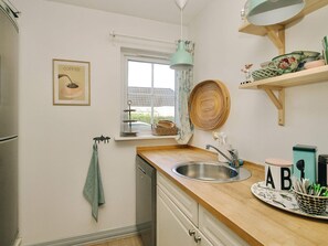 A kitchen with a sink, a window with a view, a hanging light fixture, and a shelf with kitchenware. - 4 Star Holiday Home in Vejby (Vejby)