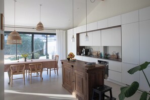 A modern kitchen with white cabinets, a wooden island, pendant lights, and a dining area with a table and chairs.