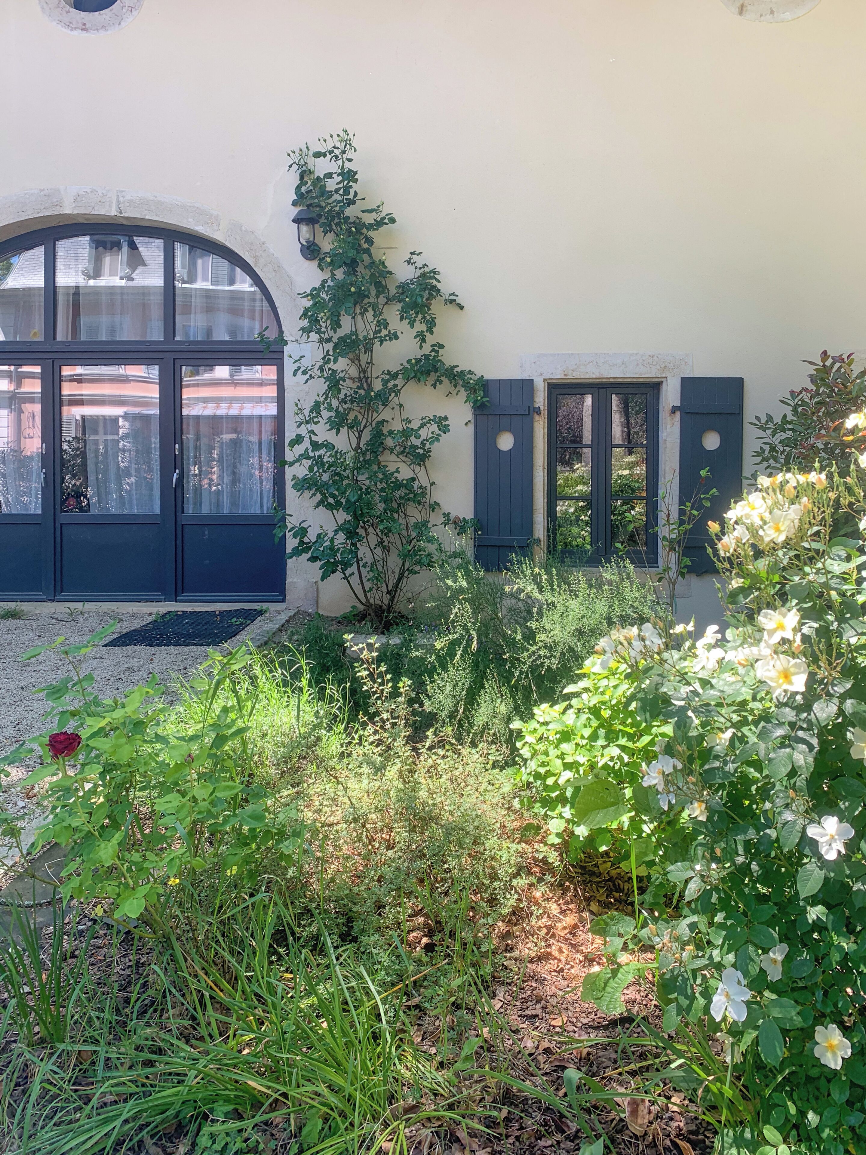 A courtyard with a building featuring a large arched window, a door, and a small window with shutters.