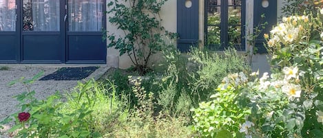 A courtyard with a building featuring a large arched window, a door, and a small window with shutters.