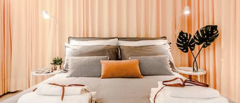 A neatly made bed with multiple pillows and a bedside table with a plant.