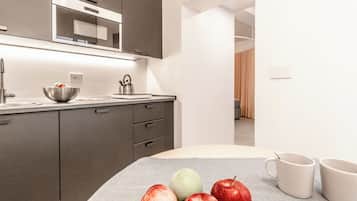 Une cuisine moderne équipée d’un four à micro-ondes, d’une bouilloire et d’un saladier rempli de fruits, posé sur le plan de travail.