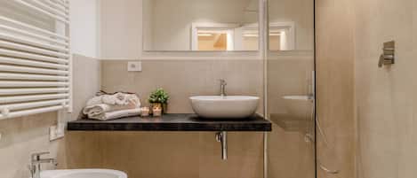 Un baño moderno con una bañera independiente, un lavamanos con lavabo sobre encimera y una ducha con mampara de vidrio.