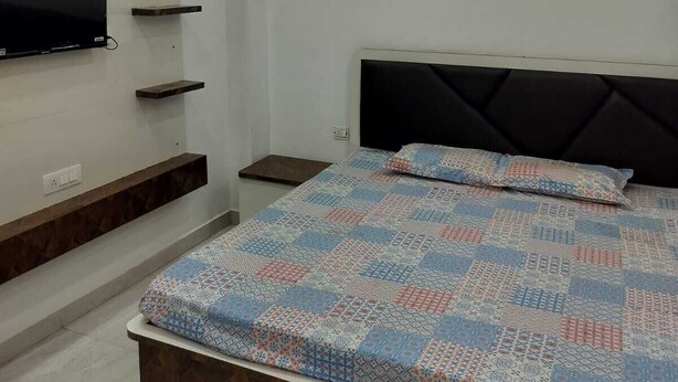 Quarto com cama, TV fixada na parede e estantes embutidas.