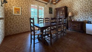 A dining area with a wooden ceiling, a chandelier, a table with chairs, a cabinet, and a window with a view. - Etxe Océan - Swimming Pool (LABENNE OCÉAN)