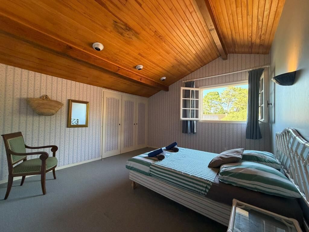 Een kamer met een houten plafond, een bed met gestreept beddengoed, een stoel en een raam met gordijnen.