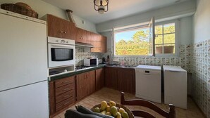 A kitchen with wooden cabinets, a microwave, a stove, a sink, and a window with a view of trees. - Etxe Océan - Swimming Pool (LABENNE OCÉAN)