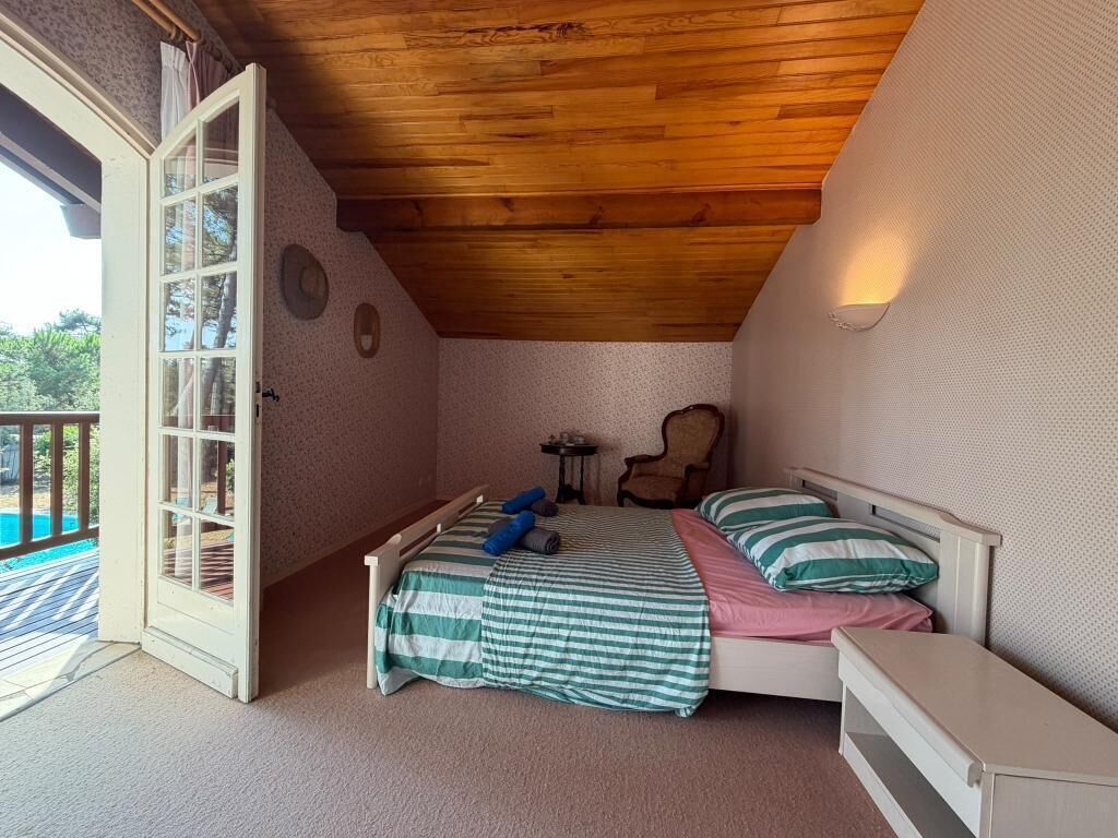Een slaapkamer met een houten plafond, een bed met gestreept beddengoed, een nachtkastje en een stoel.