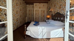 A bedroom with a bed, wooden headboard, floral wallpaper, and a nightstand with a lamp. - Etxe Océan - Swimming Pool (LABENNE OCÉAN)