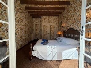 Ein Schlafzimmer mit einem Bett, einem Holzkopfstück, blumigem Wandpapier und einem Nachttisch mit einer Lampe.