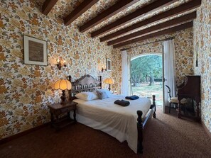 A bedroom with a bed, a nightstand, a lamp, and a window with curtains.