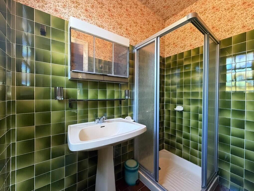 Ein Badezimmer mit grünen Fliesen, einem weißen Waschbecken und einer Duschkabine aus Glas.