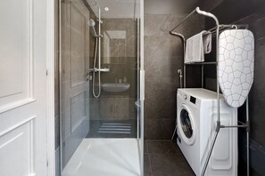 A modern bathroom with a glass shower enclosure, a built-in sink, a washing machine, and a towel rack. - URNEST Abbadia - one-bedroom apartment in the city centre (Bologna)