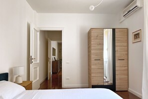 A bedroom with a bed, a bedside lamp, a wardrobe, and a door leading to another room. - URNEST Abbadia - one-bedroom apartment in the city centre (Bologna)