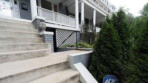 Ein zweistöckiges Haus mit Veranda, Steinstufen und einem Sicherheitshinweis.