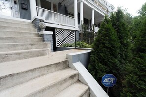 A two-story house with a front porch, a stone staircase, and a security sign. - A stylish retreat in Mount Pleasant, one of DC's most walkable neighborhoods. Two bedrooms plus a sofa bed sleep six, with two full baths - plus the city's rarest luxury: your own private off-street parking. Walk to Metro, cafes & Zoo. (Washington)