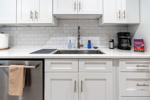 A kitchen with white cabinets, a stainless steel sink, a coffee maker, and a bag of coffee.
