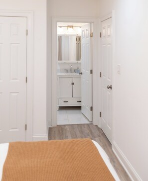 A narrow hallway leading to a bathroom with a mirror, sink, and cabinets.