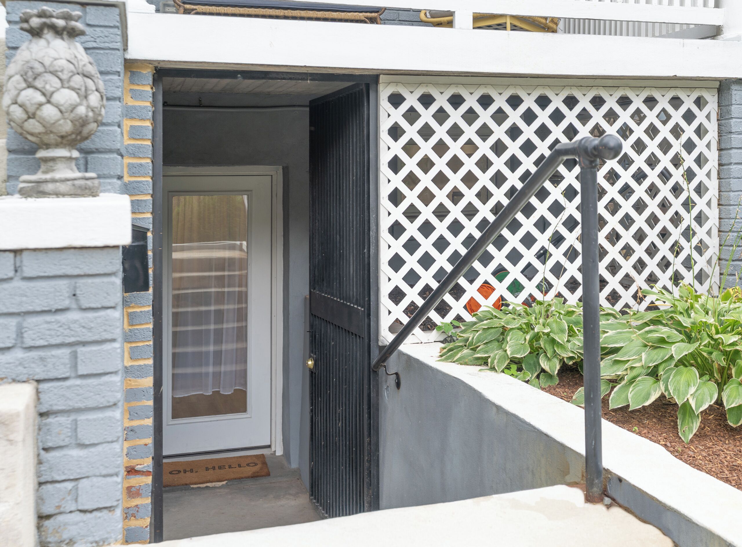 A residential entrance with a closed door, a white lattice fence, and a potted plant.