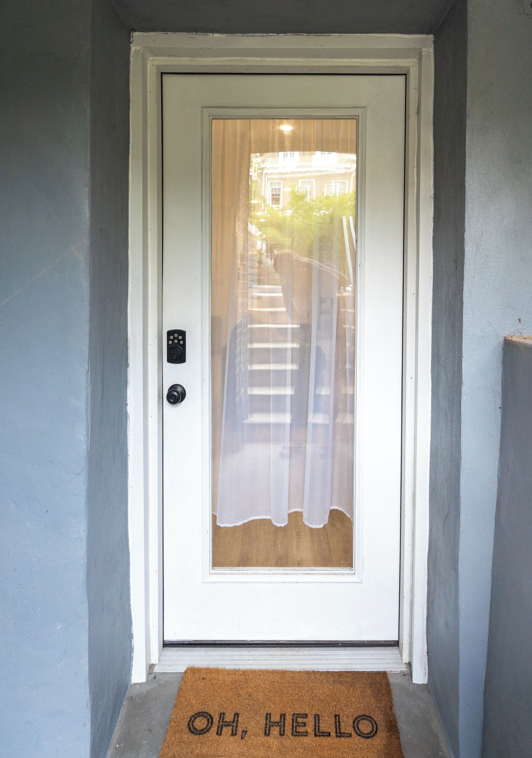 A white door with a frosted glass panel and a doormat with 'OH HELLO' written on it.