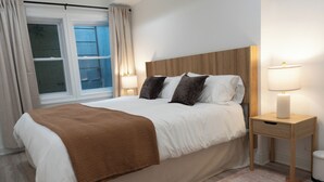 Ein ordentlich bezogenes Bett mit einer braunen Decke, einem hölzernen Kopfteil, Nachttischlampen und einem Fenster mit Vorhängen.